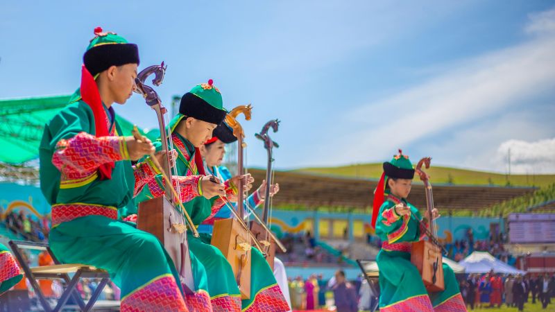 Mongoolse muzikanten in traditionele kleding die de morin khuur bespelen tijdens het Naadam festival.